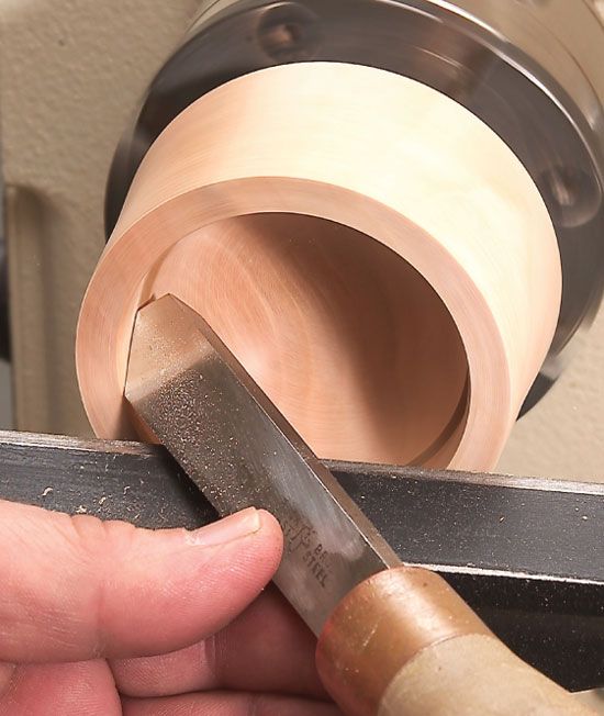 a person is working on a piece of wood with a small metal object in the background