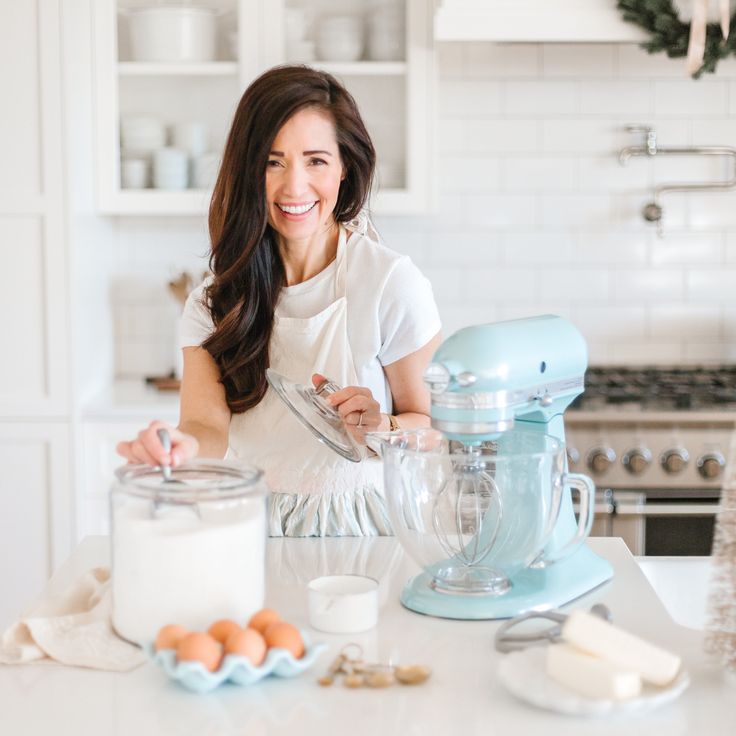 a woman standing in front of a kitchen counter with an electric mixer and ingredients on it