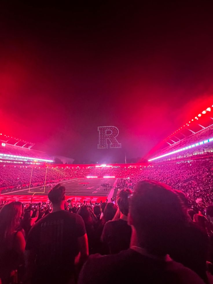 a large crowd at a concert with red and pink lights in the dark sky above them