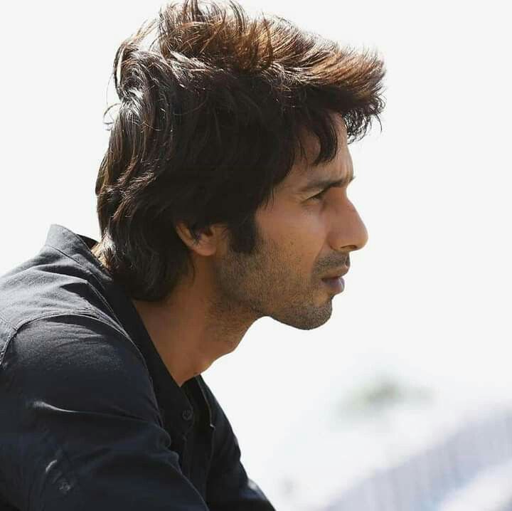 a man with long hair sitting down looking off to the side and wearing a black shirt