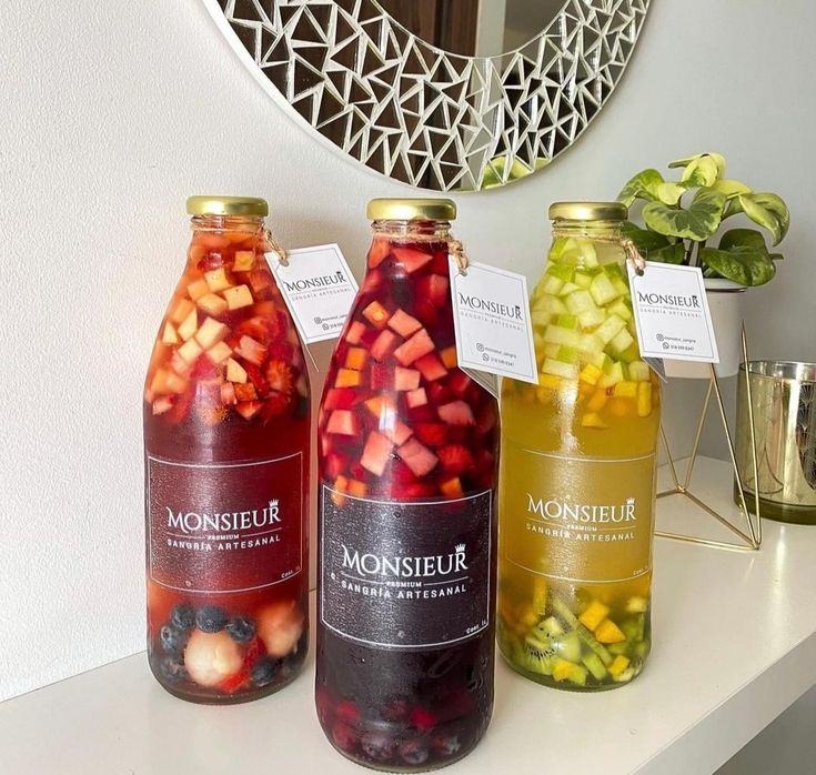 three jars filled with different types of fruit sitting on top of a white shelf next to a mirror