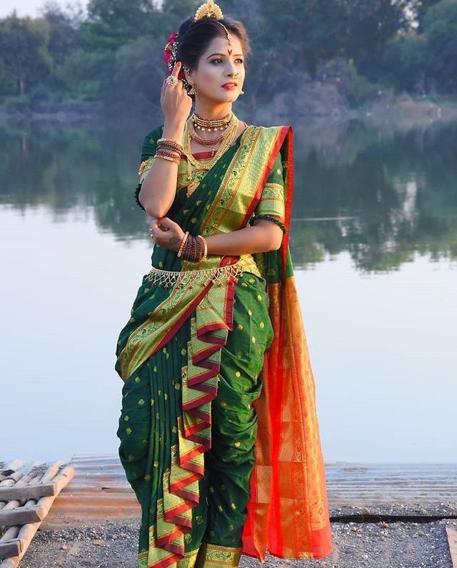 a woman in a green and orange sari is standing by the water with her hand on her ear