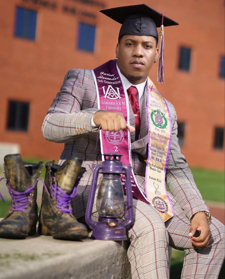 a man in a suit and tie sitting on a ledge with his graduation cap over his head