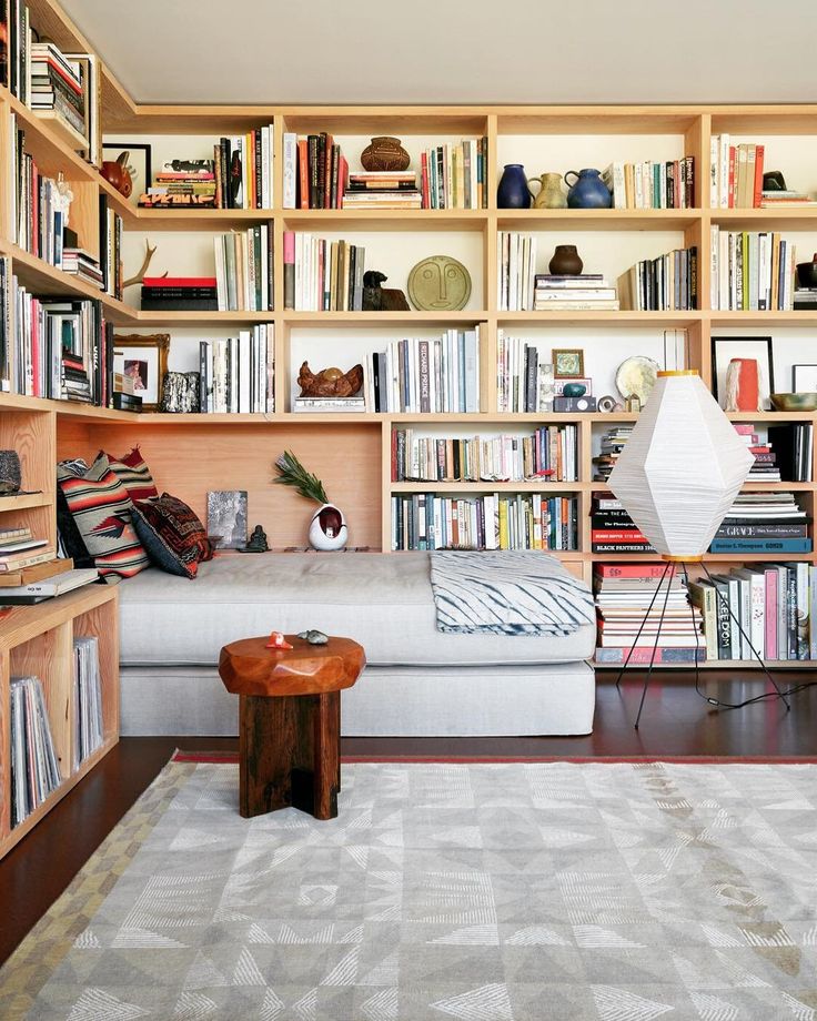 a living room filled with lots of books and furniture next to a white rug on top of a hard wood floor