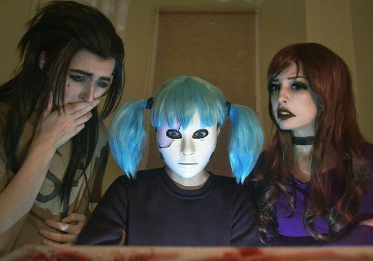 three people with blue hair and makeup are looking at a cell phone while wearing creepy masks