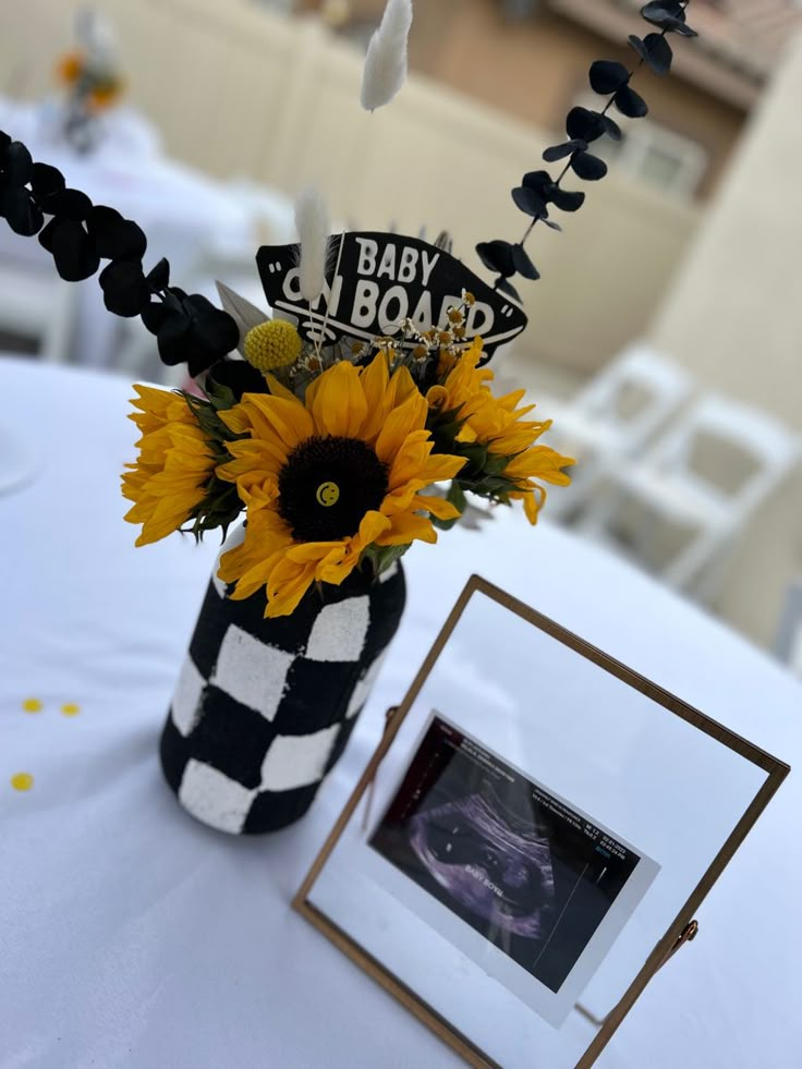 a vase filled with sunflowers on top of a table next to a framed photo