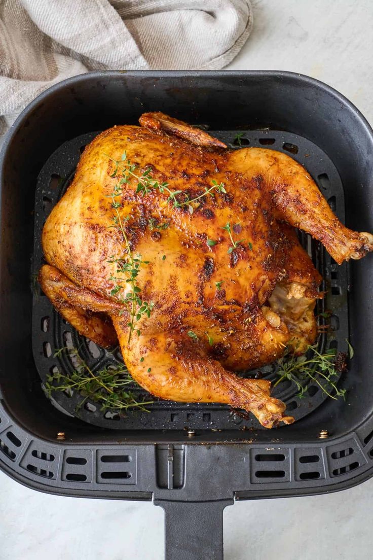 a roasted chicken in a roasting pan with herbs