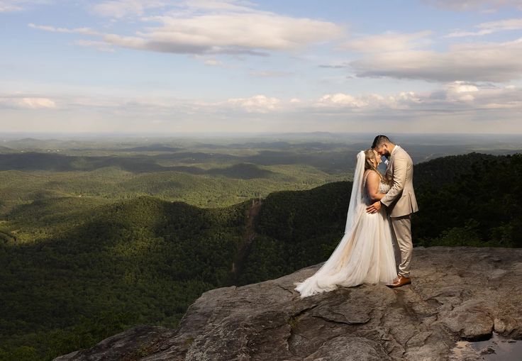 a bride and groom kissing on top of a mountain