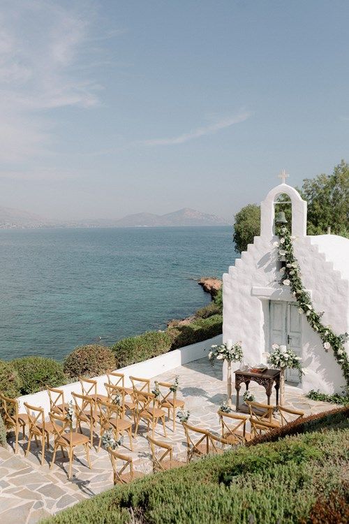 an outdoor wedding set up on the side of a building overlooking the ocean with greenery