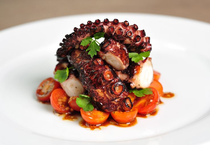 an octopus dish on a white plate with tomatoes