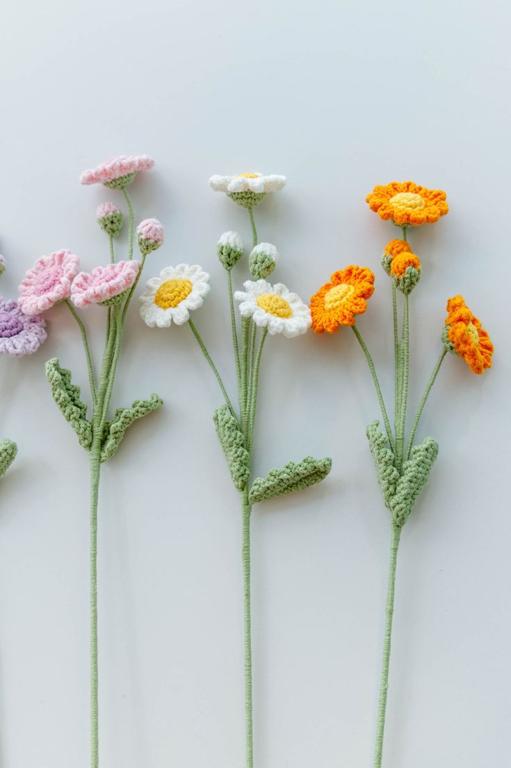 five crocheted flowers are arranged on a white surface, one is yellow and the other is pink