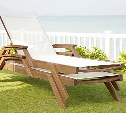 a wooden lounge chair sitting on top of a lush green field next to the ocean