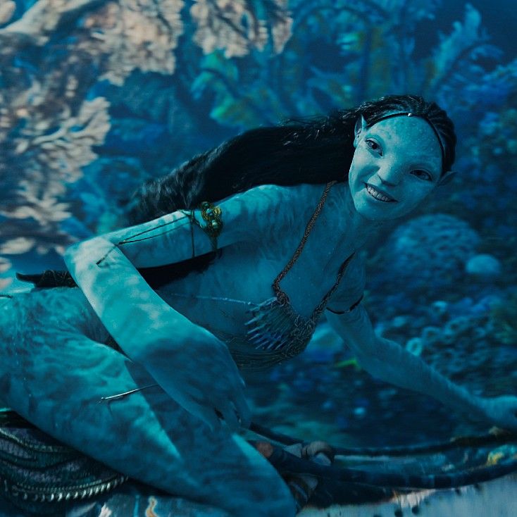 a woman with white paint on her face and body, sitting in front of an aquarium