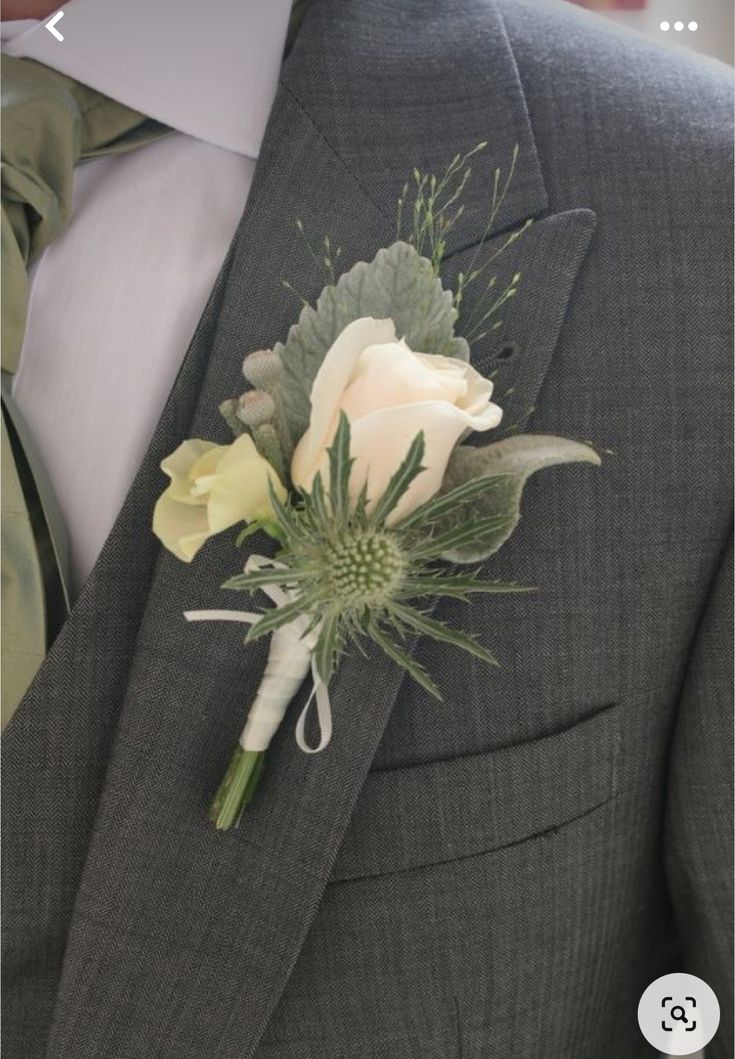 a boutonniere with white flowers and greenery on the lapel of a man in a suit