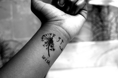 a black and white photo of a woman's arm with a dandelion tattoo on it