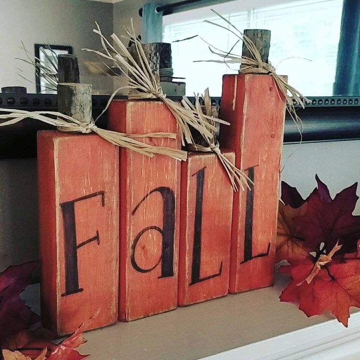 a wooden block with the word fall written on it next to some fake leaves and twine