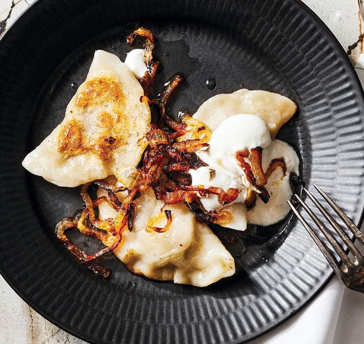 a black plate topped with dumplings covered in sauce and toppings next to a fork