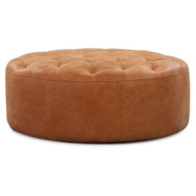 a round leather ottoman sitting on top of a white floor