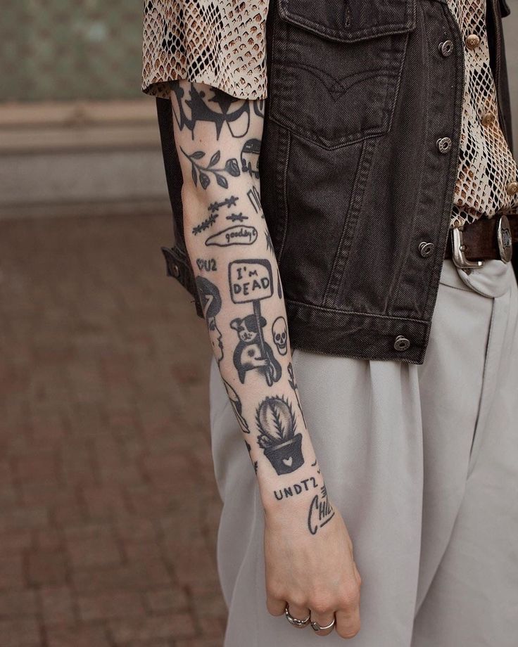 a man with tattoos on his arm and hand is wearing a black denim vest over white pants