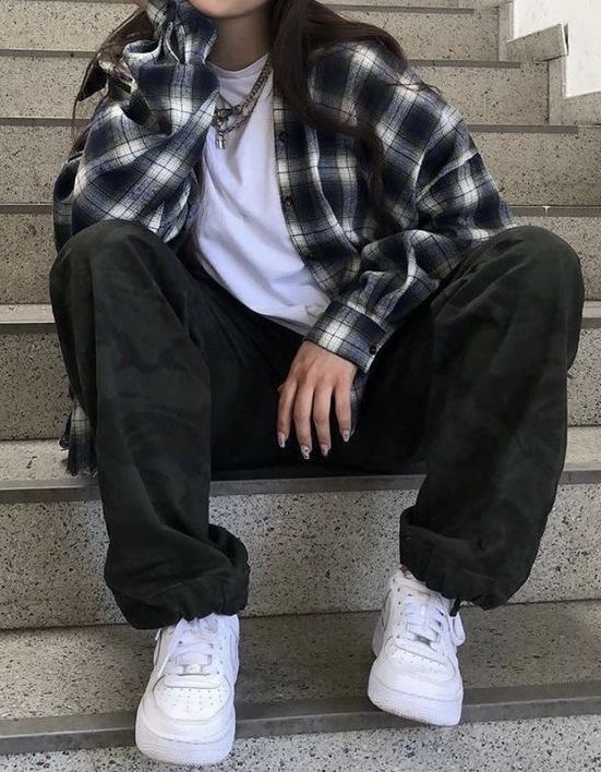 a person sitting on some steps with their feet crossed and wearing white sneakers, black pants and a plaid shirt