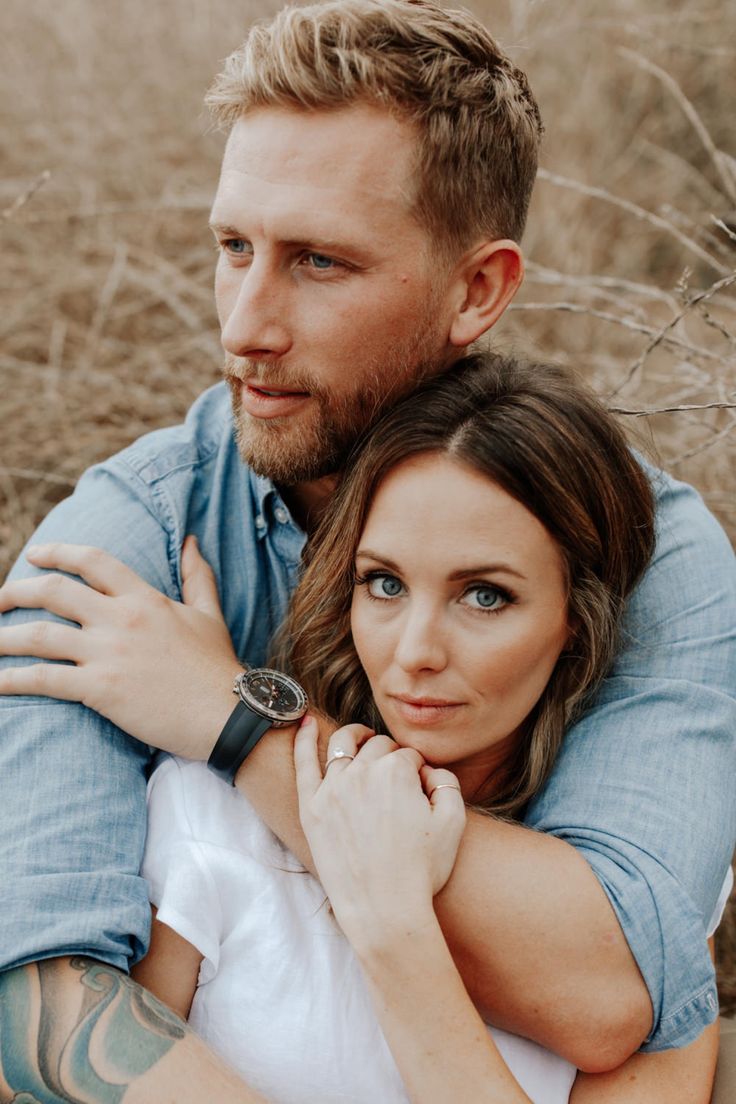 a man and woman sitting next to each other in the grass with their arms around each other