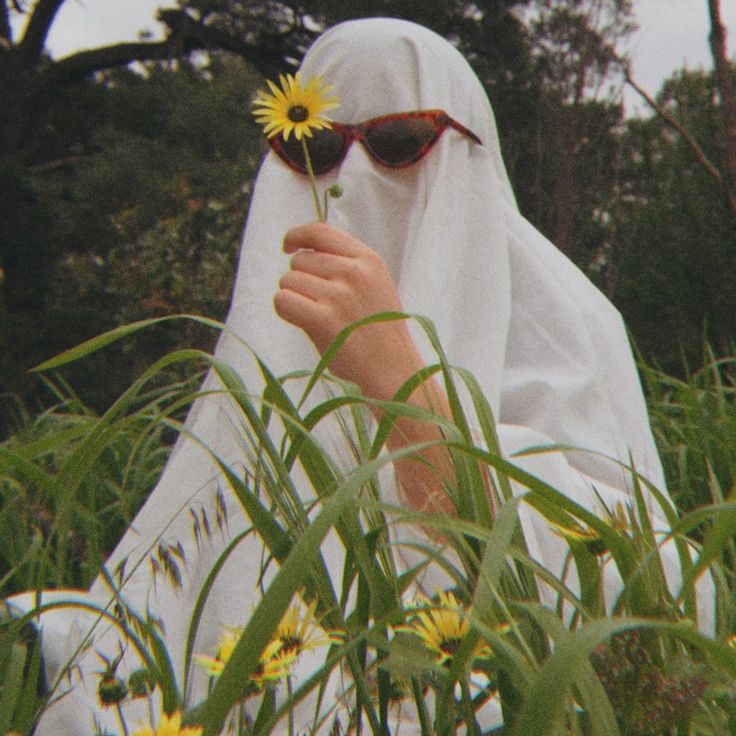 a woman in a white veil and sunglasses holding a yellow flower up to her face