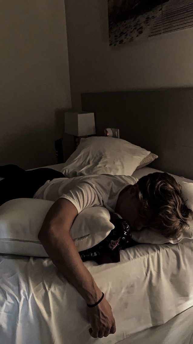 a man laying on top of a white bed in a bedroom next to a window