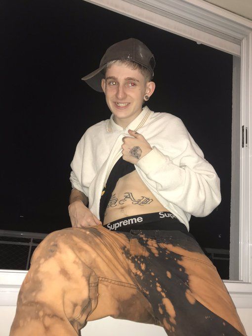 a young man sitting on top of a window sill wearing a hat and sweatpants