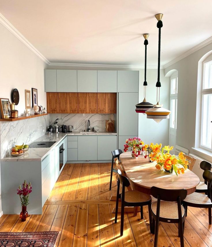 a kitchen and dining room with hardwood floors, white cabinets and wooden table surrounded by chairs