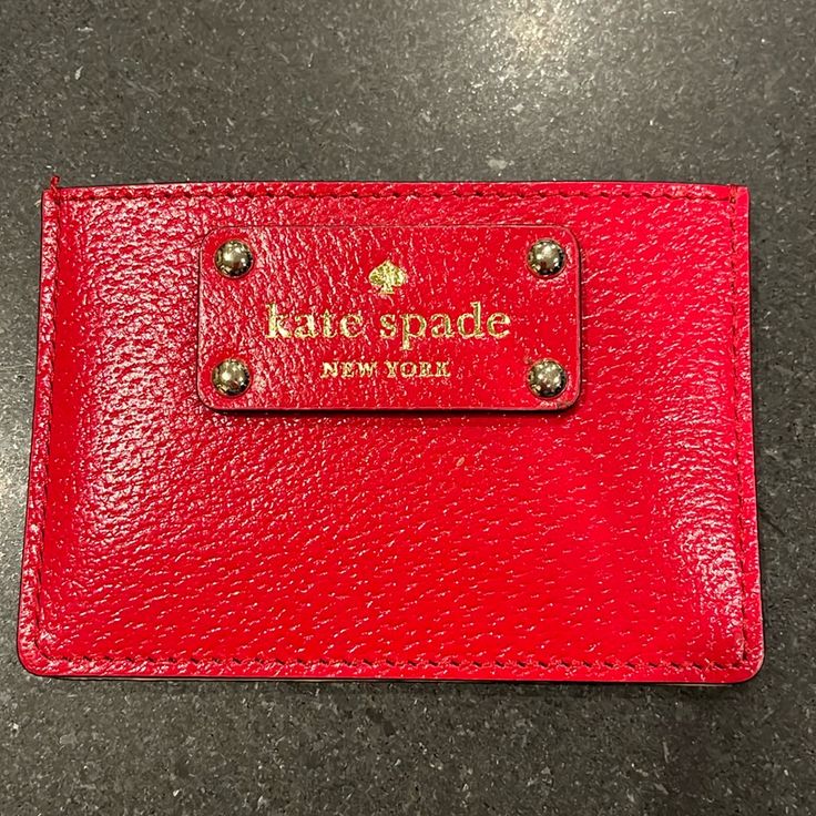 a red card case with the name kate spade on it sitting on a black surface