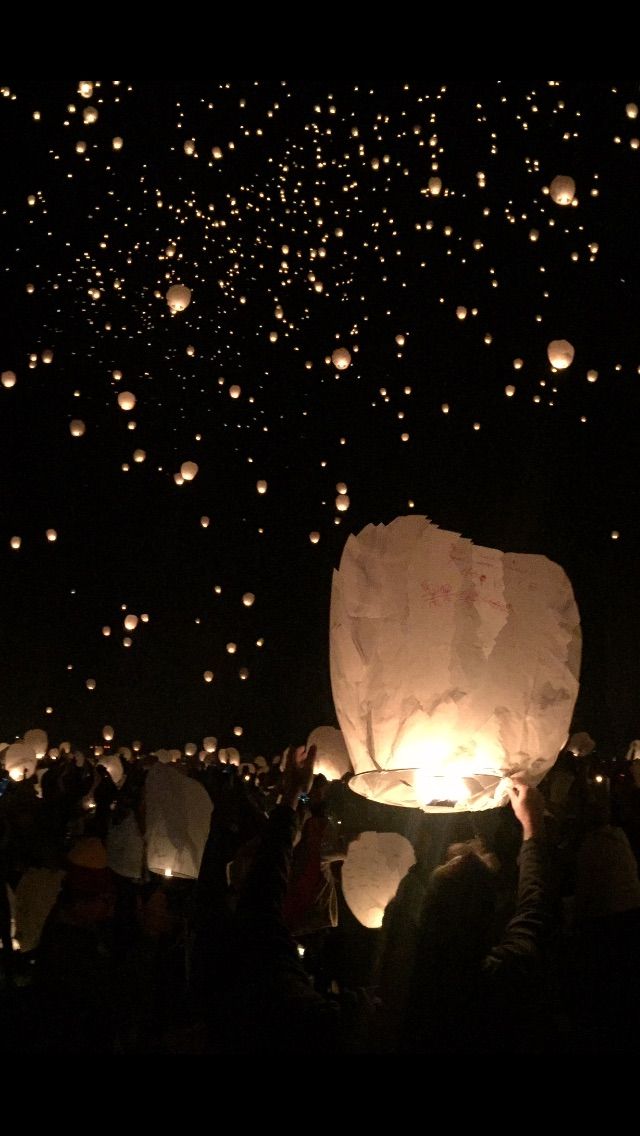 many people are flying lanterns in the dark sky at night with lights shining on them