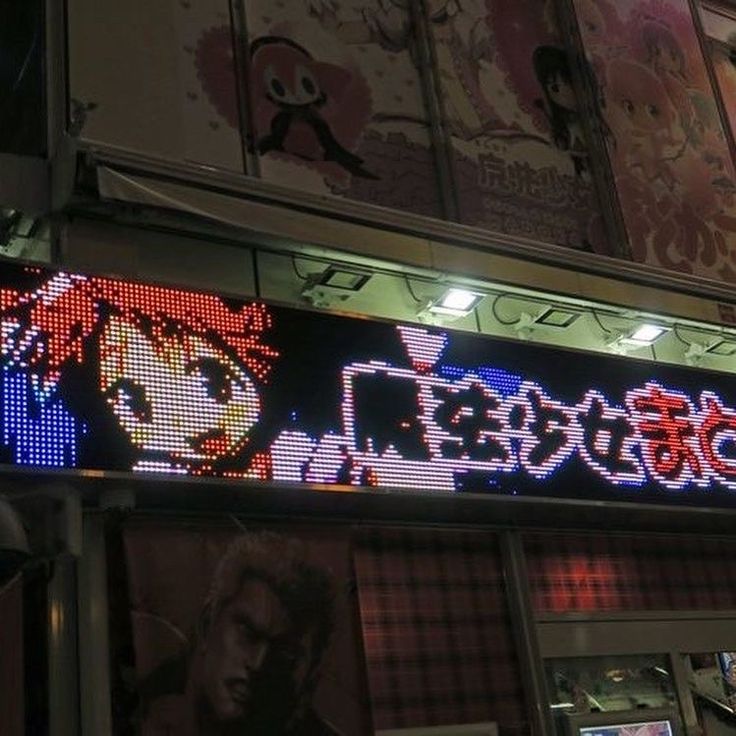 an illuminated sign on the side of a building at night with anime characters painted on it