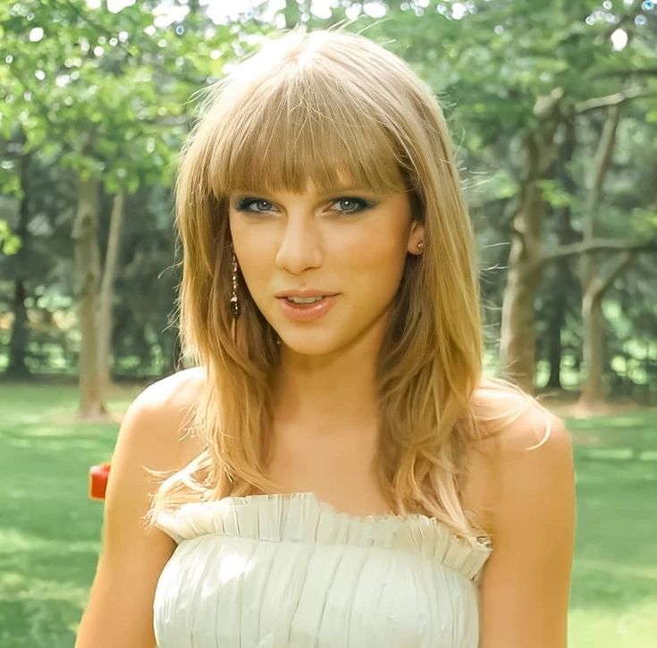 a woman in a white dress holding her hand out to the side with trees in the background