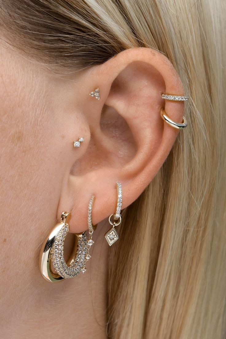 a woman wearing three different types of ear piercings in gold and silver, with diamonds on them