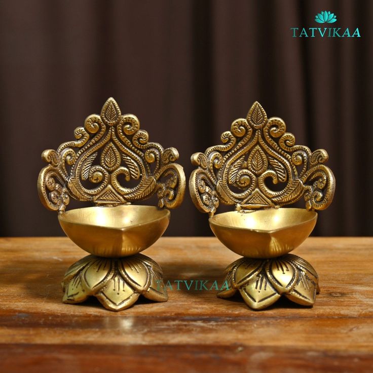 two golden bowls sitting on top of a wooden table next to each other with ornate designs