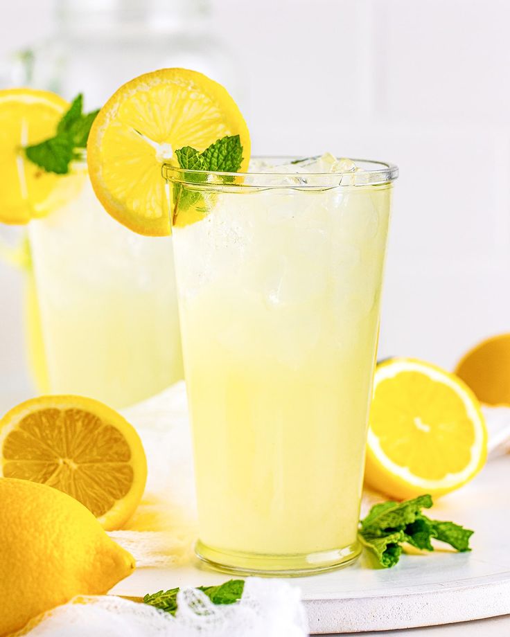 two glasses filled with lemonade and garnished with mint on a white surface