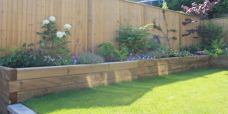 a wooden garden bed in the middle of a yard with flowers growing on it's sides