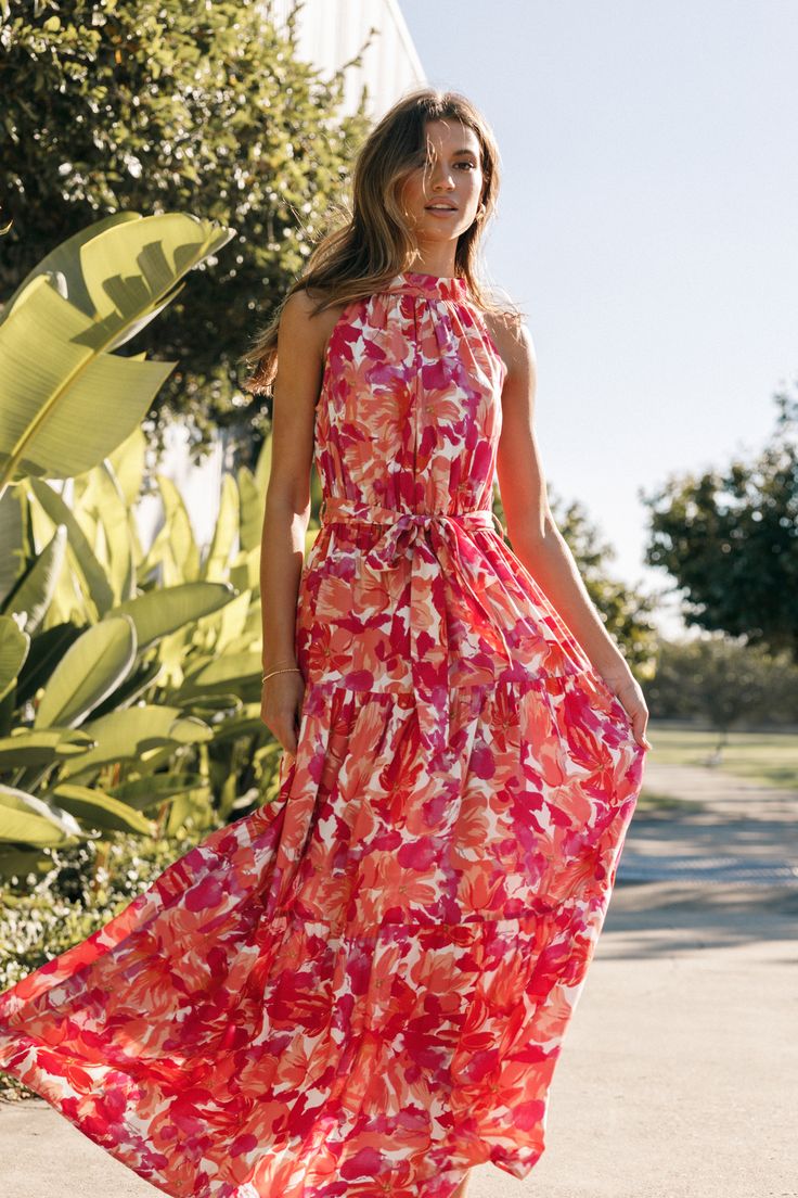 a woman in a red and pink dress is walking down the street with her hand on her hip