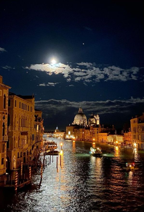 the full moon is shining in the night sky over some buildings and boats on the water