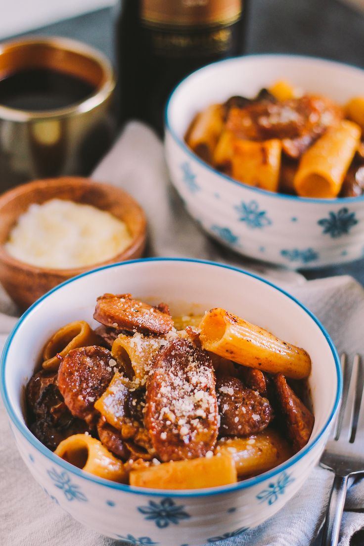 two bowls filled with pasta and meat on top of a table next to silverware