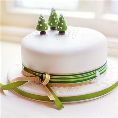 a white cake with green ribbon and small trees on top