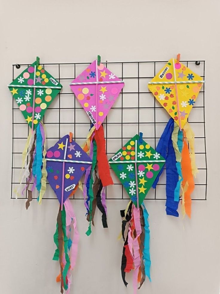 four colorful kites hanging from a wire rack on the wall in front of a white wall