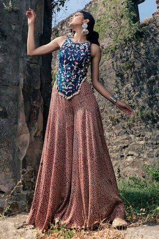 Peach flared palazzo with indigo blue and pink printed motifs. Paired with blue backless top featuring embroidered details with thread, mirror and zardozi work.
Component: 2
Pattern: Embroidered, Printed
Type Of Work: Zardozi, Mirror and Thread Embroidery
Neckline: Round
Sleeve Type: Sleeveless
Fabric: Raw Silk, Silk
Color: Peach, Blue
Other Details: 
Cowry shell tassel details
Backless multi strap tie-ups
Occasion: Destination Wedding - Aza Fashions Printed Skirt Top Indian Outfit, Skirt Top Indian Outfit, Palazzo And Top, Cape Skirt, Flared Palazzo, Trendy Outfits Indian, Anamika Khanna, Traditional Indian Dress, Casual Indian Fashion