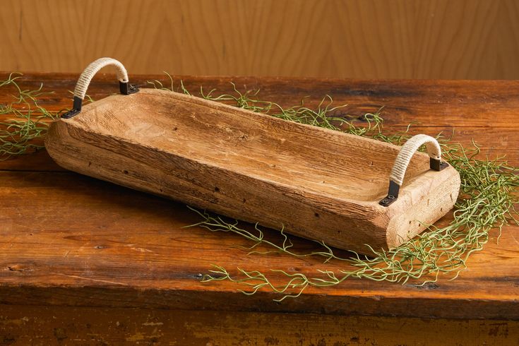 a wooden tray with two handles and some grass in it sitting on a table next to a wall