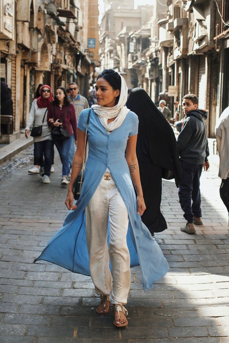 a woman is walking down the street in a blue dress and white pants with an angel wings on her head