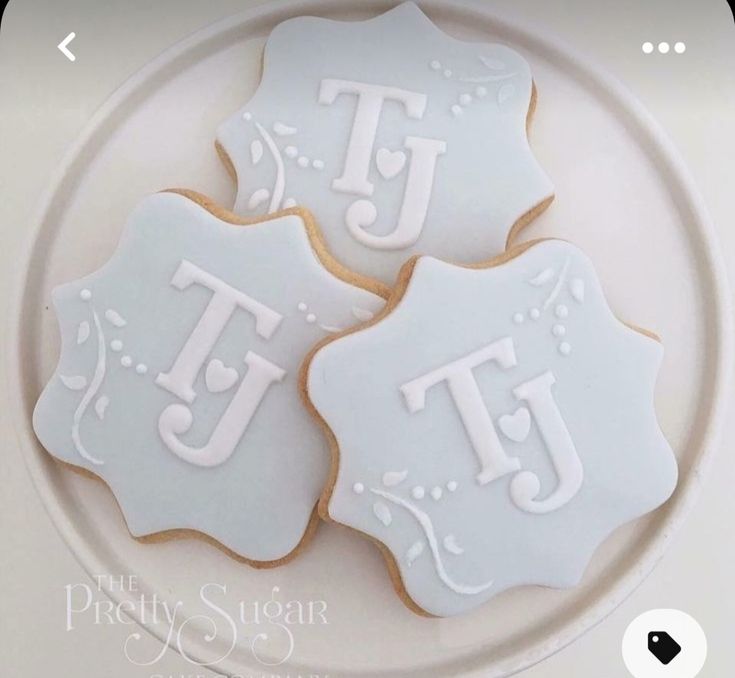 three decorated cookies on a plate with the letters t and j in white icing