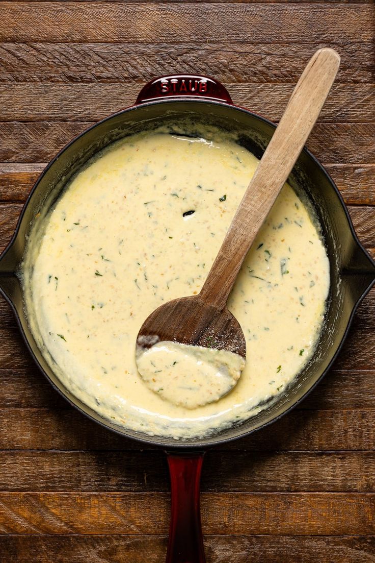 a wooden spoon in a pan filled with cheese sauce on top of a wood table