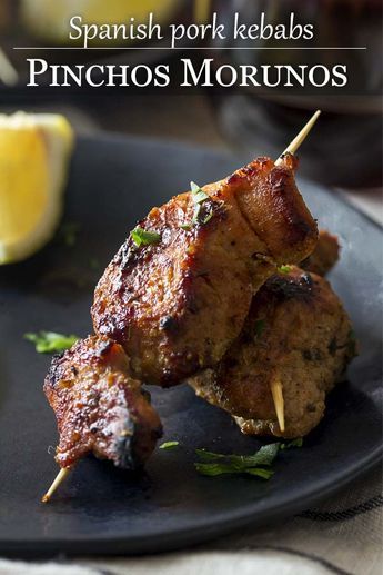 two skewered meats are on a black plate with lemon wedges in the background