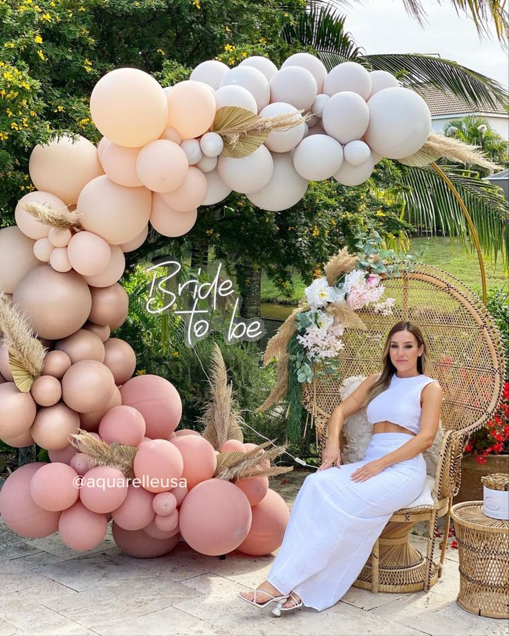 a woman sitting on a wicker chair in front of a backdrop with balloons and flowers