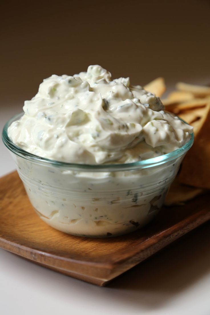 a small glass bowl filled with whipped cream and crackers on a wooden platter